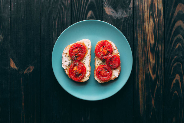 Twee boterhammen met boter en tomaten bestrooid met specerijen op een bord. Houtachtergrond. - Foto, afbeelding