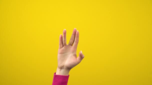 女性の手にエイリアンの挨拶記号が表示されます。孤立した黄色の背景のスタジオ写真. - 映像、動画