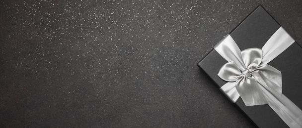 Musta lahjapakkaus, jossa on hopeanauha ja suuri rusetti graniitin tummalla taustalla. Paikka kirjoitukselle - Valokuva, kuva