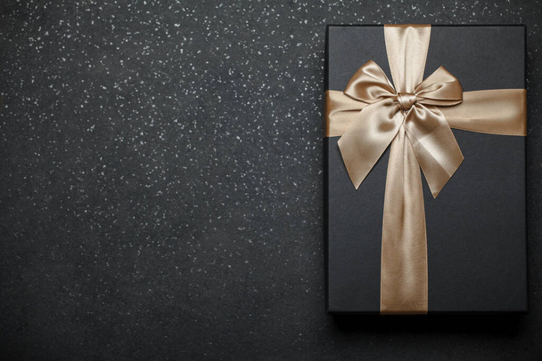 Fekete ajándékdoboz arany szalaggal és egy nagy masnival gránit sötét háttérrel. A felirat helye - Fotó, kép