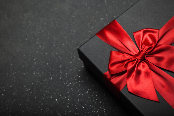 Musta lahjapakkaus, jossa on punainen nauha ja suuri rusetti graniittisella tummalla taustalla. Paikka kirjoitukselle - Valokuva, kuva