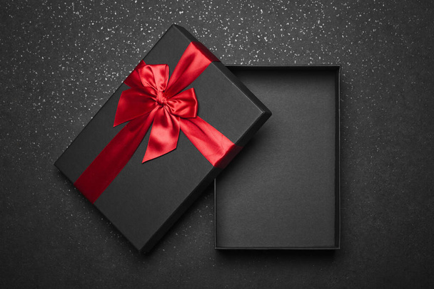 Opened black gift box with a red ribbon and a large bow on a dark granite surface. Empty box. Mockup - Photo, Image