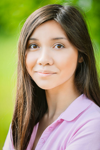 Una bella giovane donna di aspetto asiatico, con i capelli scuri e una camicetta rosa su sfondo verde natura estiva. - Foto, immagini