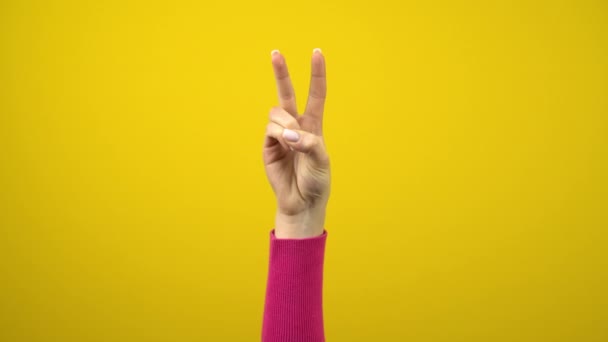 Το γυναικείο χέρι δείχνει το σημάδι ειρήνης ή νίκης. Φωτογραφία στούντιο σε ένα απομονωμένο κίτρινο φόντο. - Πλάνα, βίντεο