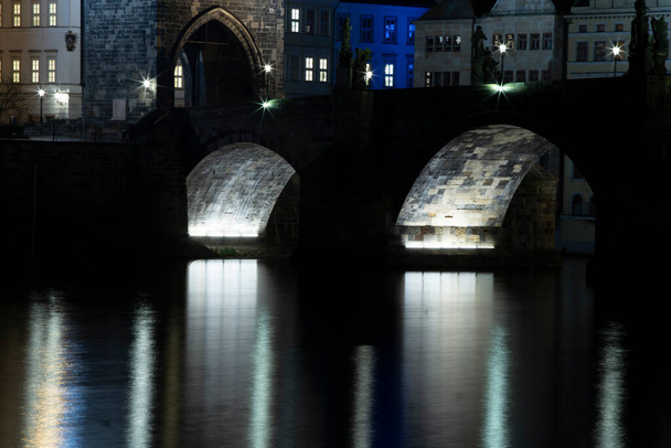 oświetlenie Mostu Karola z 14 wieków i światło z oświetlenia ulicznego i kamienne rzeźby na moście i odbicia światła na powierzchni rzeki Wełtawy w nocy w Pradze - Zdjęcie, obraz