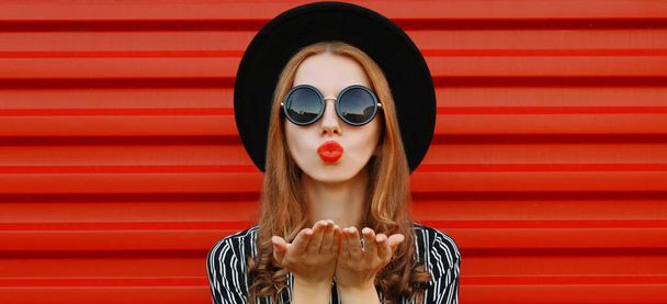 Portrait close up of attractive woman blowing red lips sending sweet air kiss over red wall background - Φωτογραφία, εικόνα