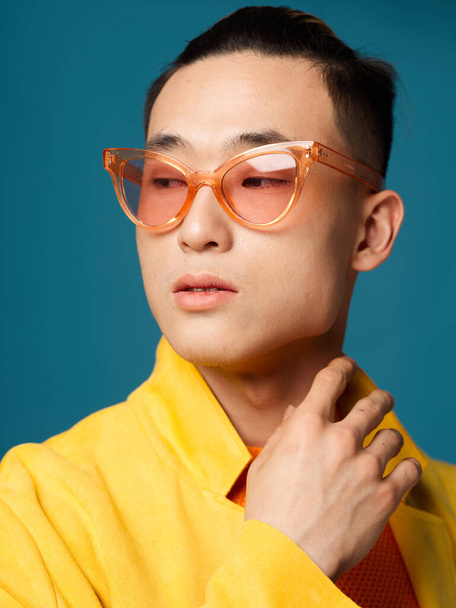 Retrato de um homem com óculos aparência asiática casaco amarelo fundo azul - Foto, Imagem