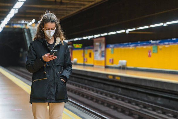 New normal. Young girl using her smartphone in the subway. Teenager using her smartphone in the subway. Teenager with a mask. Young girl with protective mask. Pandemic. - Zdjęcie, obraz