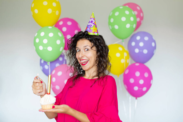 Happy Birthday. Sexy brunette girl posing with balloons, fireworks, colorful balloons and holiday cake on a white background. - Fotó, kép
