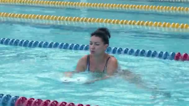 Женщина тренирует аква-гимнастику с гантелями из пенопласта в бассейне. - Кадры, видео