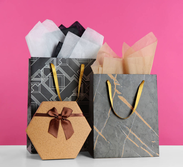 Gift bags with paper on white table against pink background - Foto, imagen