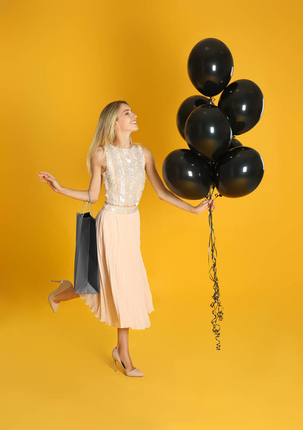 Happy young woman with balloons and shopping bag on yellow background. Black Friday Sale - Foto, Imagem