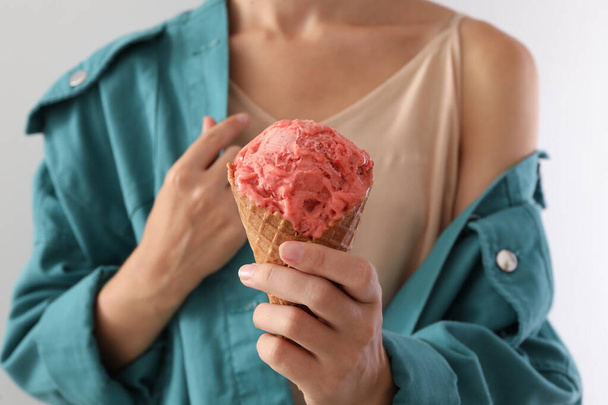 Woman holding pink ice cream in wafer cone on light grey background, closeup - 写真・画像