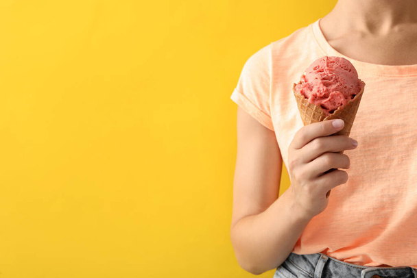 Nainen, jolla on vaaleanpunaista jäätelöä kiekkokartiossa keltaisella pohjalla, lähikuva. Tekstitila - Valokuva, kuva