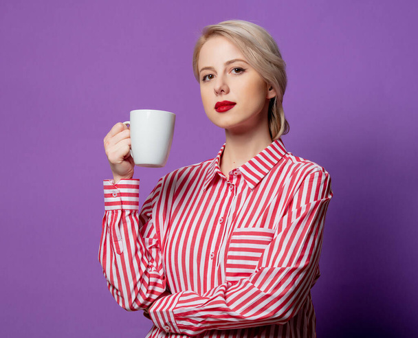 Beautiful woman in red striped shirt with cup of coffee on purple background - Foto, Imagem