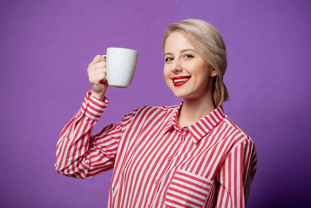 Piękna kobieta w czerwonych paskach z filiżanką kawy na fioletowym tle - Zdjęcie, obraz