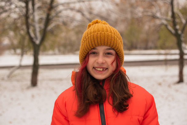 een meisje in een fel oranje warme jas. Meisje in een oranje jasje bij slecht weer. Tiener meisje in de winter - Foto, afbeelding