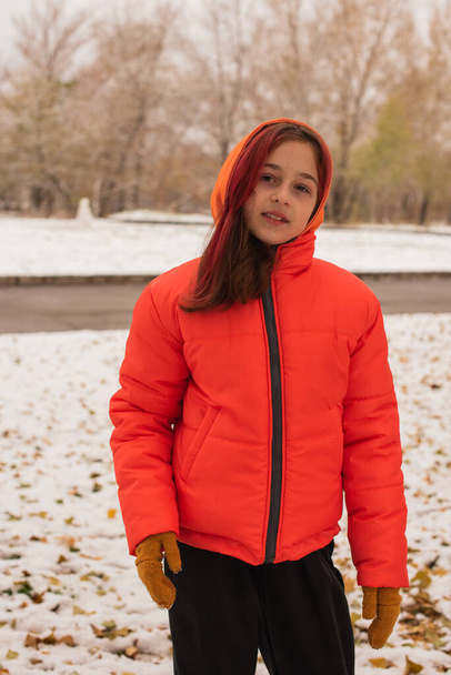 een meisje in een fel oranje warme jas. Meisje in een oranje jasje bij slecht weer. Tiener meisje in de winter - Foto, afbeelding