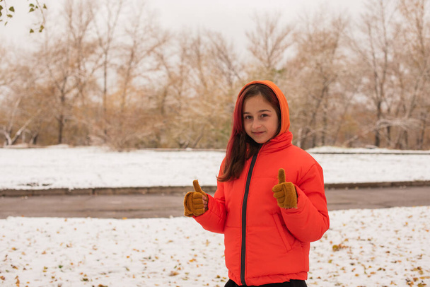 a girl in a bright orange warm jacket . Girl in an orange jacket in snowy weather. Teenager girl in winter - Photo, Image