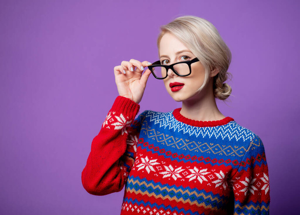 Mooie vrouw in Kerst trui en bril op paarse achtergrond - Foto, afbeelding