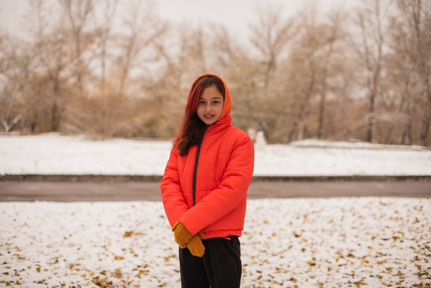 Dziewczyna w pomarańczowej, ciepłej kurtce. Dziewczyna w pomarańczowej kurtce w śnieżnej pogodzie. Nastolatka w zimie - Zdjęcie, obraz