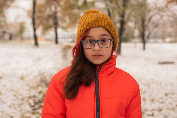 Tyttö kirkkaan oranssissa lämpimässä takissa. Tyttö oranssissa takissa lumisella säällä. Teini tyttö talvella - Valokuva, kuva