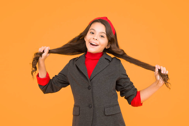 Happy small kid in school uniform hold long brunette hair locks yellow background, salon - Фото, зображення