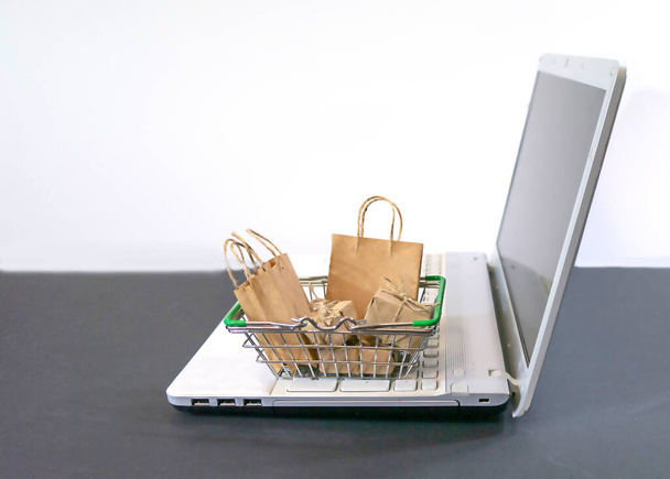 Shopping cart with groceries on laptop keyboard on white background, selective focus. Ordering products online, Copy space - Photo, Image