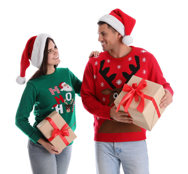 Beautiful happy couple in Santa hats and sweaters holding Christmas gifts on white background - Fotografie, Obrázek