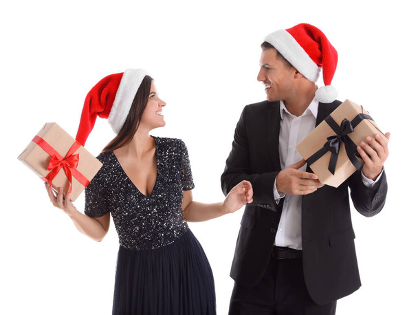 Beautiful happy couple in Santa hats holding Christmas gifts on white background - Foto, Bild