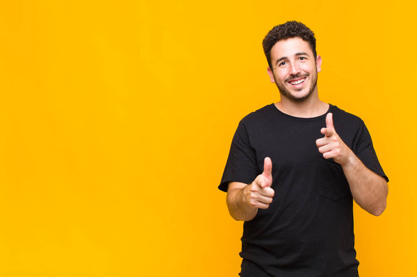 young man smiling with a positive, successful, happy attitude pointing to the camera, making gun sign with hands - Φωτογραφία, εικόνα