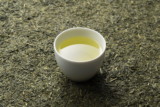 Feuilles de thé posées sur l'écran. Thé vert dans une tasse de thé blanc placé sur elle. Image de style japonais - Photo, image