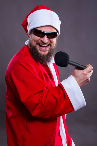 Bearded rocke with micriphome dressed in Santa Claus costume - 写真・画像