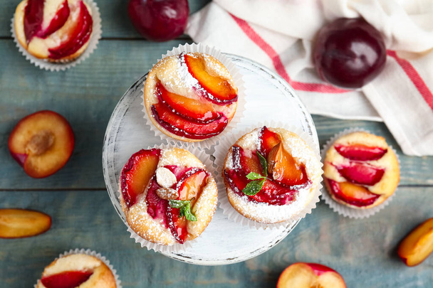 Delicious sweet cupcakes with plums on wooden stand, flat lay - Фото, зображення