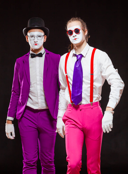 Portrait of male mime artists, isolated on black background. Two men wearing bright purple and pink suits go straight to the camera. Symbol of confident, brutal, cool - Photo, image