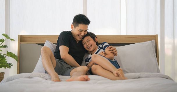 asian dad and son have good time talking and playing together on bed at home. concept father and son relationship and father day. selective focused - Фото, изображение