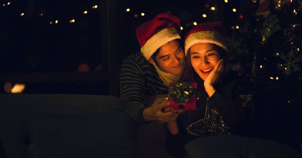 アジア人の恋人夫婦はクリスマスとお正月のお祝いの夕食に男が女性に与える贈り物と一緒に壮大な瞬間を持っています。クリスマスと大晦日の夫婦関係の概念 - 写真・画像