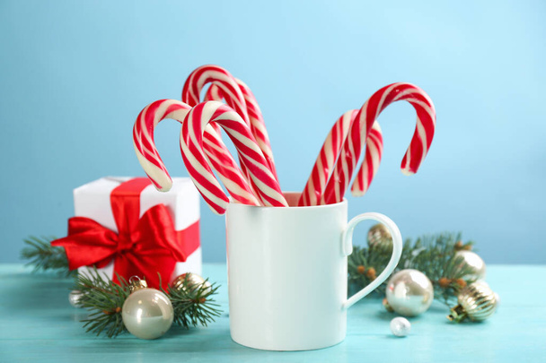 Many sweet candy canes in cup and Christmas decor on light blue wooden table - 写真・画像