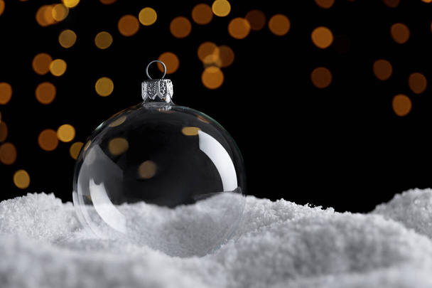 Transparent Christmas ball on snow against blurred fairy lights, space for text - Foto, immagini