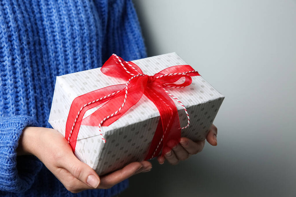 Woman holding white Christmas gift box on grey background, closeup - 写真・画像