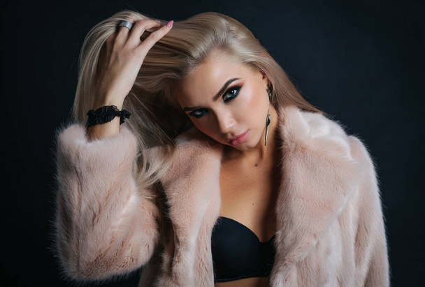 Portrait of a young woman in a fur coat with beautiful professional makeup on a dark background, - Photo, image