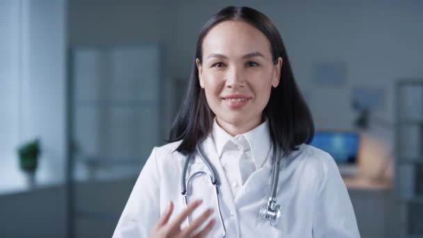Pecho arriba retrato filmado de encantadora médica asiática vistiendo un abrigo blanco sonriendo a la cámara - Imágenes, Vídeo