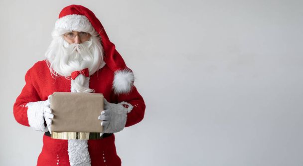 Święty Mikołaj trzyma pudełko z prezentem w rękach. Stoi w pobliżu miejsca na tekst. - Zdjęcie, obraz