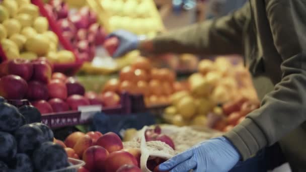 Jovem com luvas azuis coloca granadas vermelhas frescas no saco de cordas no mercado - Filmagem, Vídeo