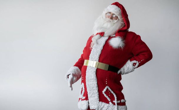Santa Claus está de pie sobre blanco, sostiene su mano detrás de su espalda. concepto de dolor de espalda. - Foto, Imagen