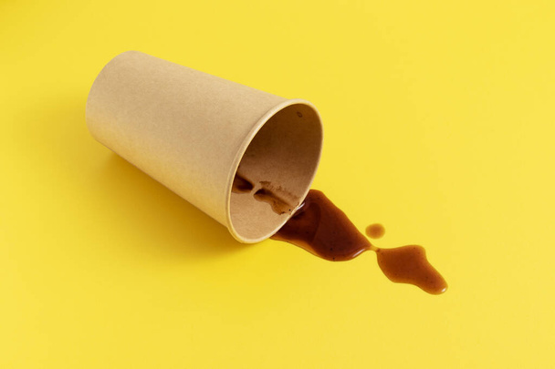 Черный кофе, пролитый из упавшей одноразовой бумажной чашки на желтом фоне. - Фото, изображение