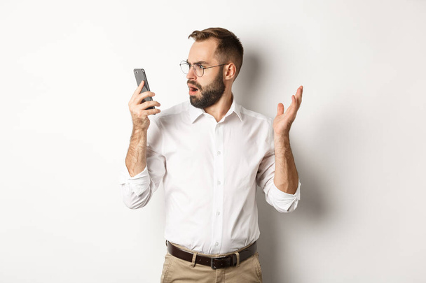 会話の後、携帯電話で混乱している男は、白い背景に困惑立っている - 写真・画像