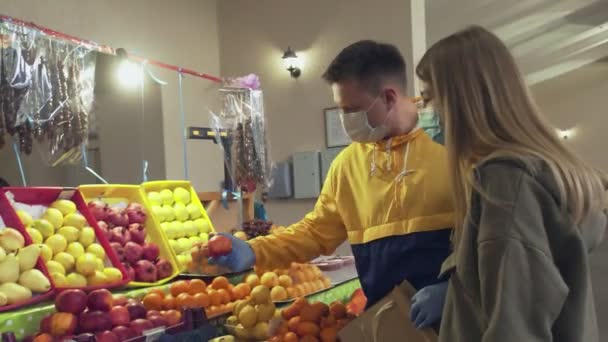 Nuori pari suojanaamarit ja käsineet valitsee hedelmiä markkinoilla - Materiaali, video