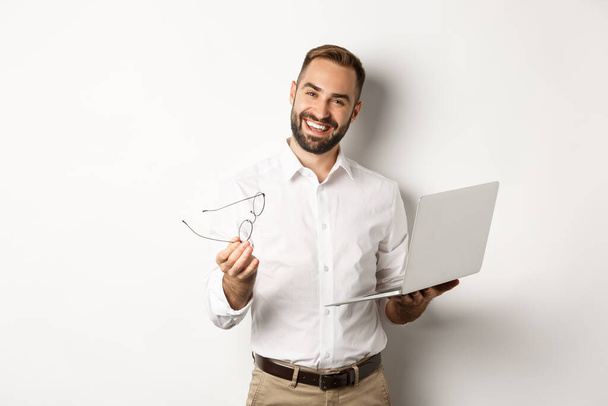 Satisfied businessman praising good job while checking laptop, standing over white background - Zdjęcie, obraz