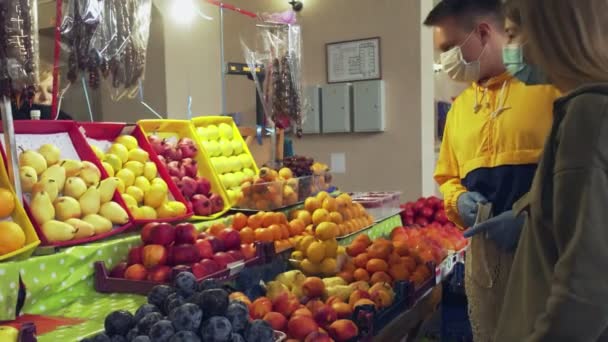 Joven pareja de máscaras protectoras y guantes elige frutas en el mercado - Metraje, vídeo